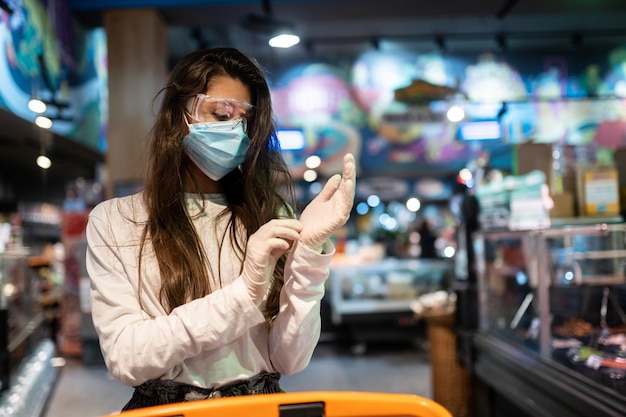 Mujer con mascarilla quirúrgica y guantes está comprando en el supermercado.