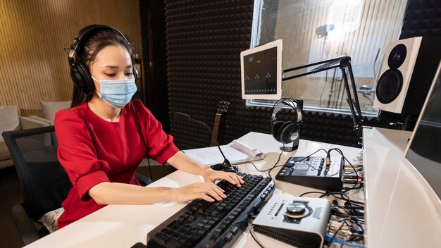 Mujer con mascarilla trabajando en radio con equipo profesional