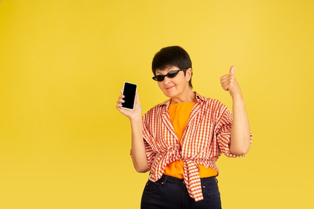 Mujer mayor aislada en amarillo. Tecnología y concepto de estilo de vida de ancianos alegre