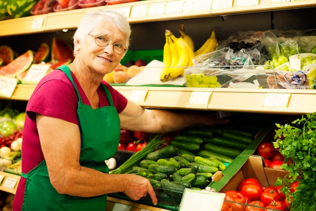 Mujer mayor arreglando verduras en la estantería