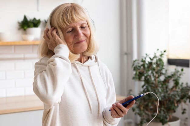 Mujer mayor con auriculares y smartphone en casa