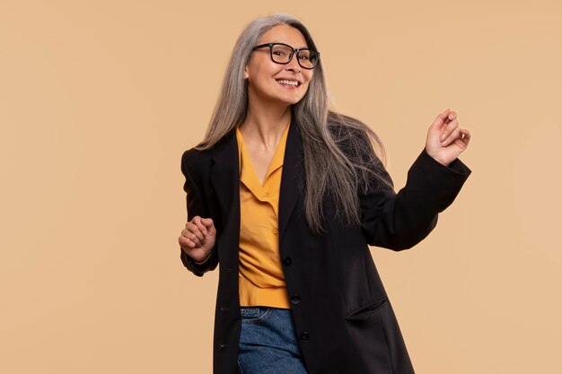 Mujer mayor bailando y usando anteojos contra un fondo amarillo