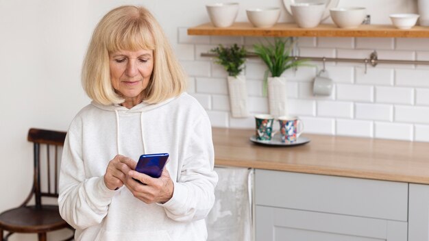 Mujer mayor en casa con smartphone con espacio de copia