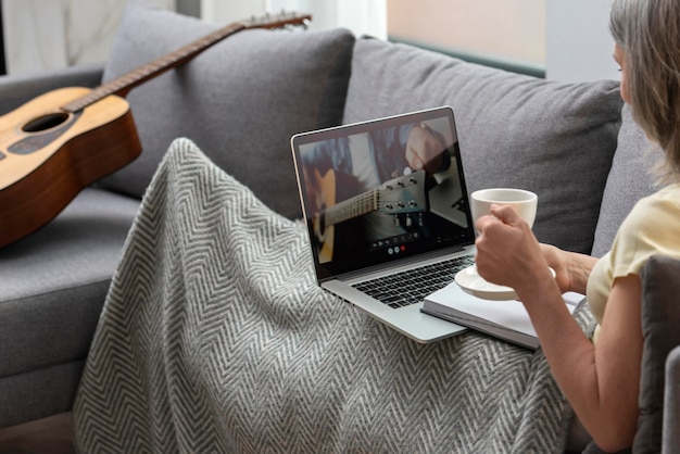 Mujer mayor en casa en el sofá usando la computadora portátil y tomando un café