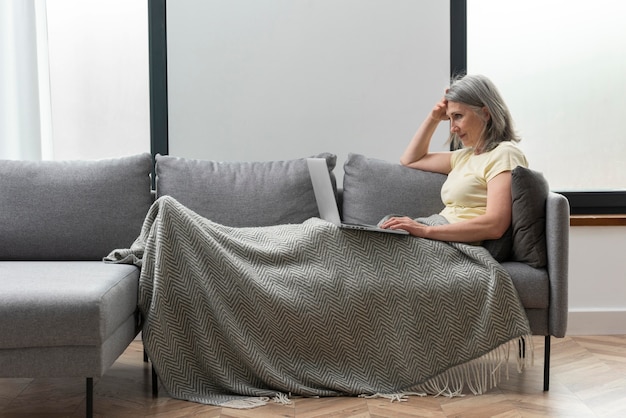 Mujer mayor, en casa, en el sofá, usar la computadora portátil