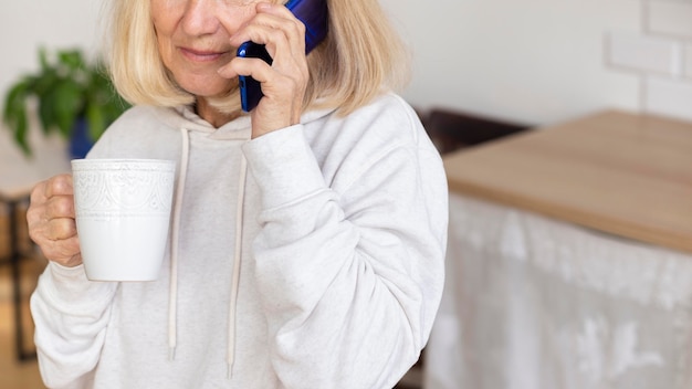 Mujer mayor en casa tomando café y hablando por teléfono