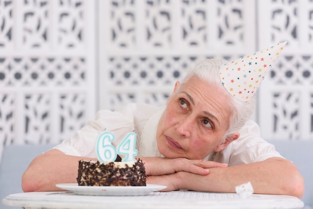 Mujer mayor contemplada que descansa su cabeza en la tabla cerca de la torta de cumpleaños