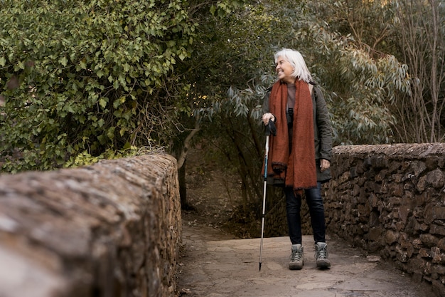 Mujer mayor cruzando un puente de piedra mientras está en la naturaleza