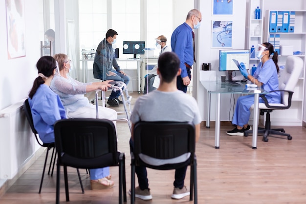 Mujer mayor discapacitada con andador sentada en la sala de espera del hospital para consulta médica contra la infección por coronavirus