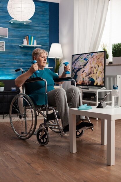 Mujer mayor discapacitada en silla de ruedas estirando los músculos de los brazos ejercitando la resistencia del cuerpo
