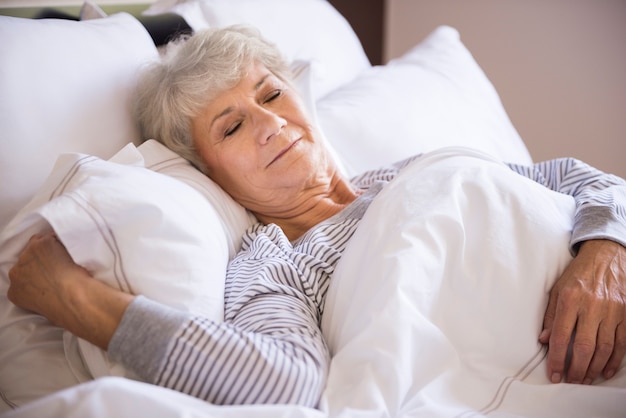 Mujer mayor durmiendo en la cama grande