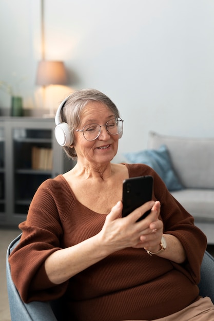 Mujer mayor escuchando música con auriculares mientras usa un teléfono inteligente