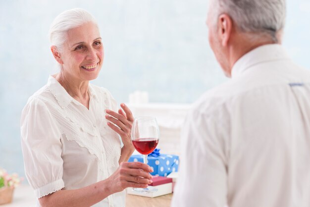 Mujer mayor feliz ofreciendo copa de vino a su marido