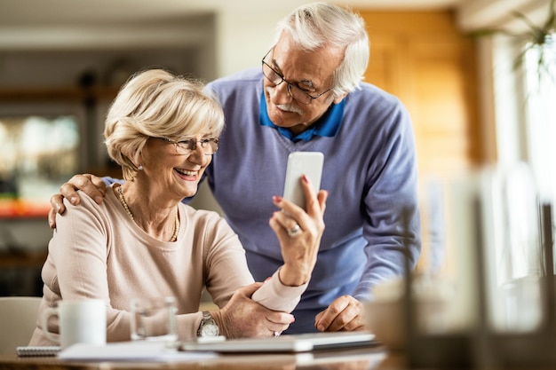 Mujer mayor feliz que usa el teléfono celular con su marido en casa