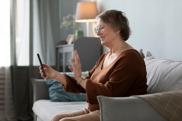 Mujer mayor feliz usando un teléfono inteligente en la sala de estar de un apartamento moderno