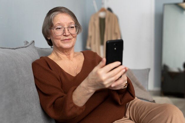 Mujer mayor feliz usando un teléfono inteligente en la sala de estar de un apartamento moderno