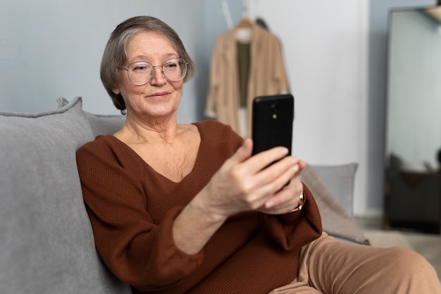 Mujer mayor feliz usando un teléfono inteligente en la sala de estar de un apartamento moderno