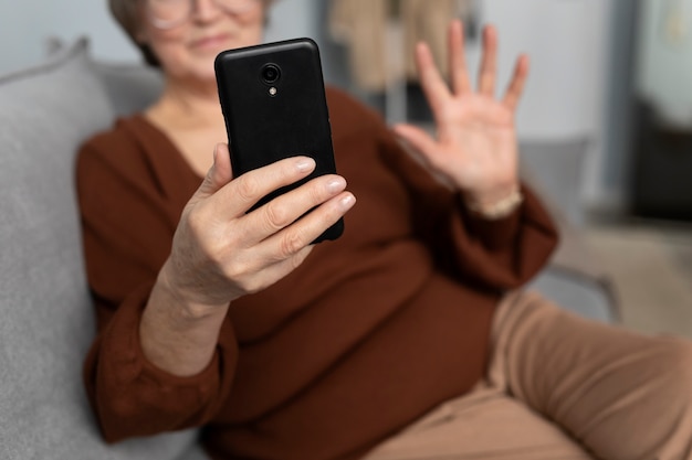 Mujer mayor feliz usando un teléfono inteligente en la sala de estar de un apartamento moderno