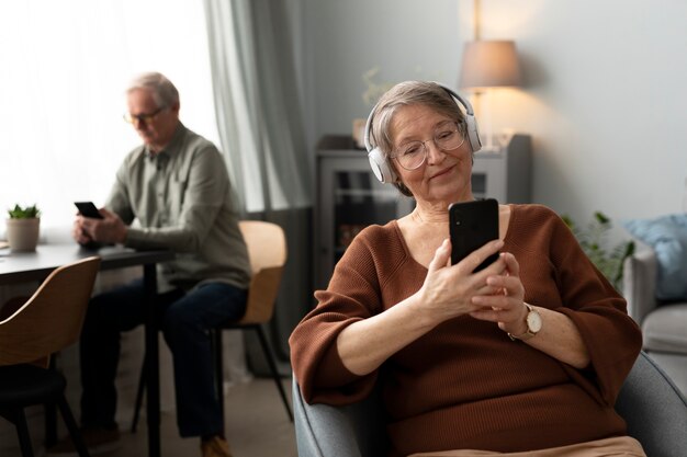 Mujer mayor feliz usando un teléfono inteligente en la sala de estar de un apartamento moderno