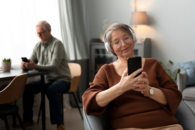 Mujer mayor feliz usando un teléfono inteligente en la sala de estar de un apartamento moderno