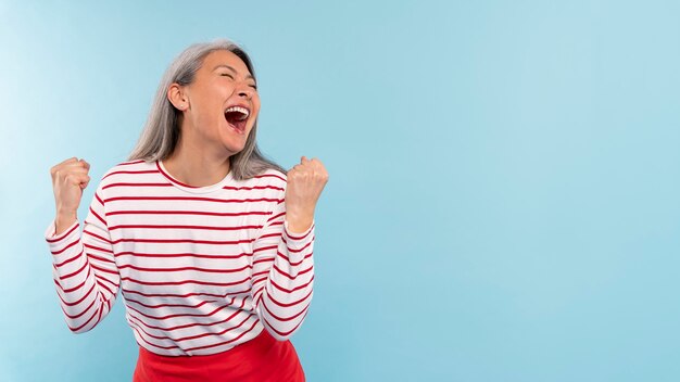 Mujer mayor gritando y emocionada contra un fondo azul