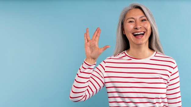 Mujer mayor haciendo el signo alienígena contra un fondo azul.