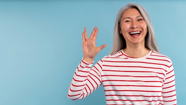 Mujer mayor haciendo el signo alienígena contra un fondo azul.