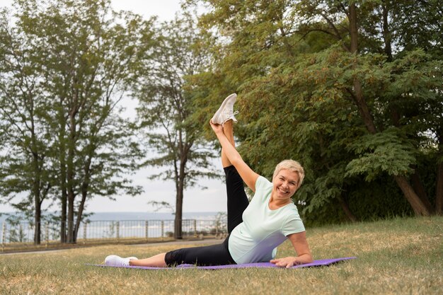 Mujer mayor haciendo yoga al aire libre en el parque