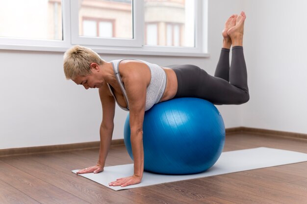 Mujer mayor en el interior haciendo ejercicios con pelota fitness