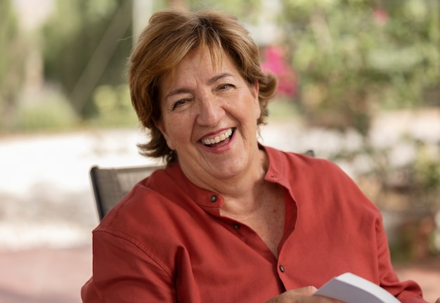 Foto gratuita mujer mayor leyendo en la naturaleza en su casa de campo y sonriendo