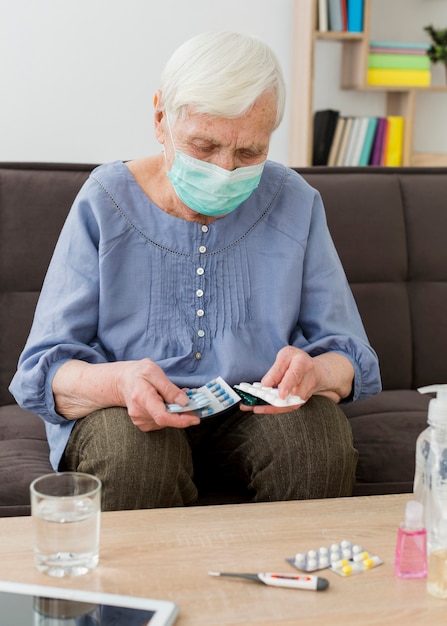 Mujer mayor con máscara médica tomando sus pastillas