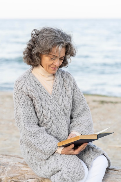 Foto gratuita mujer mayor, en la playa, lectura, un, libro
