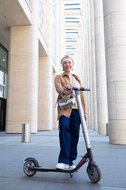 Mujer mayor posando con un scooter eléctrico en la ciudad