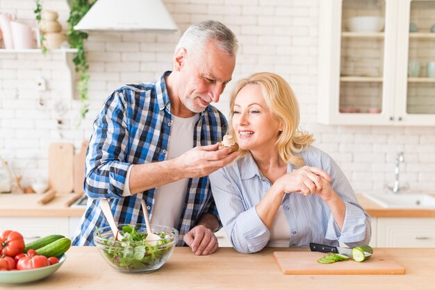 Mujer mayor que huele el asimiento de su marido en la cocina