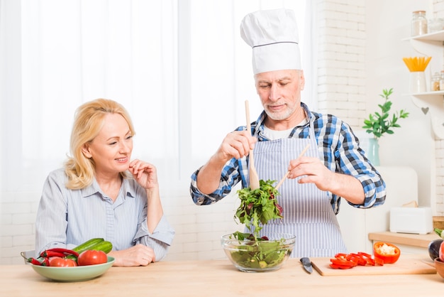 Mujer mayor que mira a su marido que prepara la ensalada en la cocina