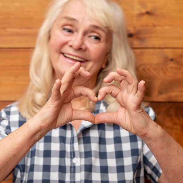 Mujer mayor que muestra la forma del corazón de la mano