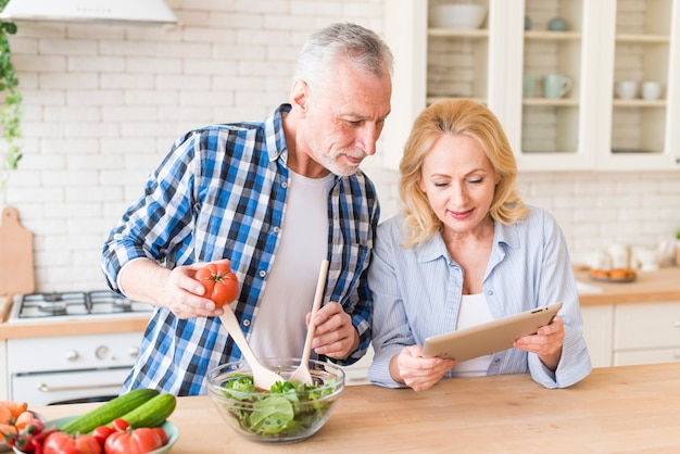 Foto gratuita mujer mayor que muestra receta a su marido que prepara la ensalada en la cocina