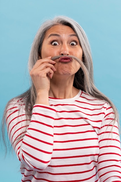 Foto gratuita mujer mayor que sostiene un bigote falso contra un fondo azul