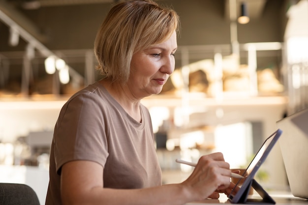 Foto gratuita mujer mayor que trabaja en su tableta en un café