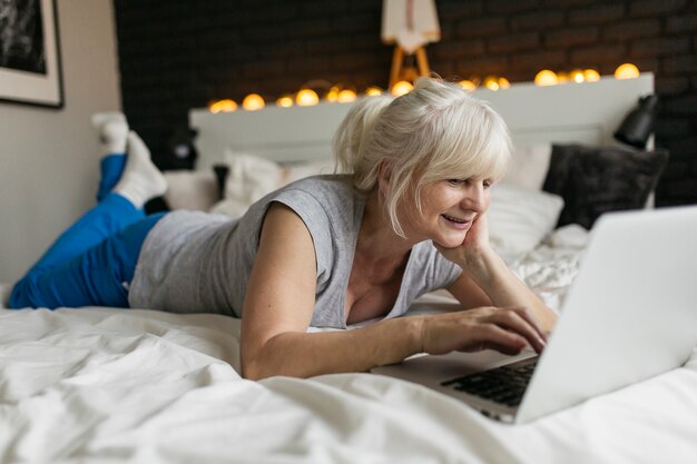 Mujer mayor que usa la computadora portátil en cama