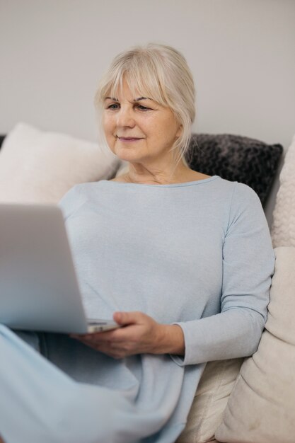 Mujer mayor que usa la computadora portátil en el sofá