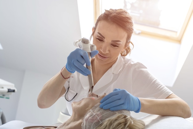 Mujer mayor recibiendo tratamiento facial con láser y ultrasonido en un centro médico