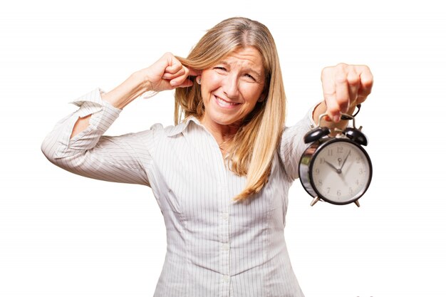 Mujer mayor con un reloj despertador haciendo como que le duele el oído