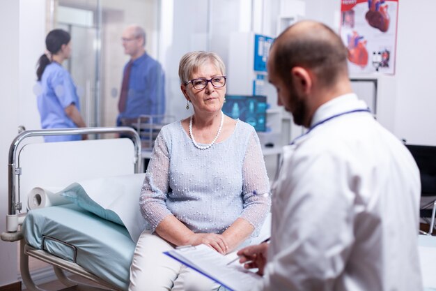 Mujer mayor respondiendo a las preguntas del médico durante el examen en la habitación del hospital