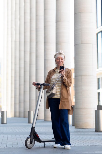 Mujer mayor con un scooter eléctrico en la ciudad con smartphone