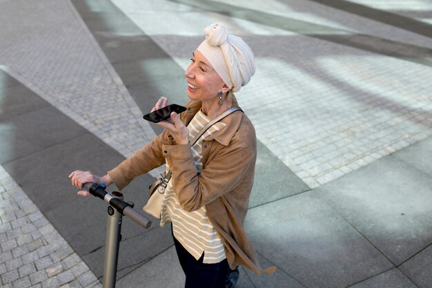 Mujer mayor con un scooter eléctrico hablando por teléfono en la ciudad