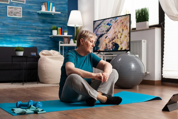 Mujer mayor sentada en posición de loto en la estera de yoga entrenando los músculos del cuerpo para adelgazar peso