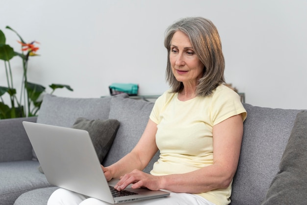 Mujer mayor, en el sofá, en casa, usar la computadora portátil