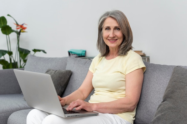 Mujer mayor, en el sofá, en casa, usar la computadora portátil