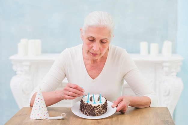 Mujer mayor sola que arregla velas en la torta de cumpleaños en casa